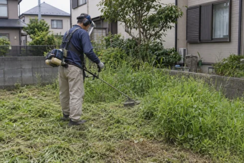日本の戸建ての庭で刈払機を使って伸びた雑草を刈る作業風景